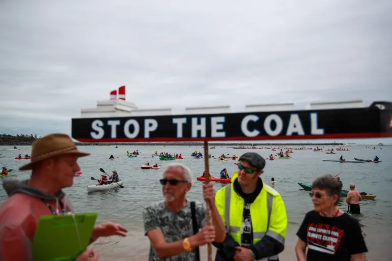 A man holds a sign reading, 'Stop the coal,' during a protest at the world's largest coal port in Newcastle, Australia [File: Roni Bintang/Getty Images]